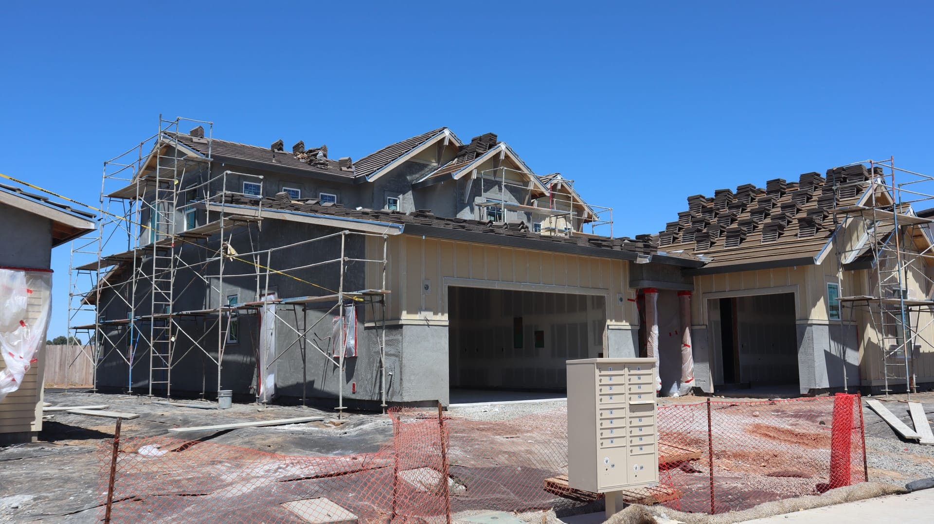 A large new-build home under construction, wrapped in scaffolding with the roof tiles being fitted